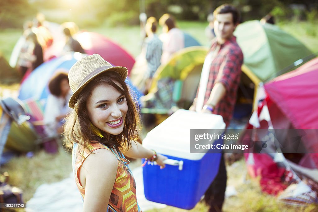 Portrait of woman helping man carry cooler outside tents at music festival