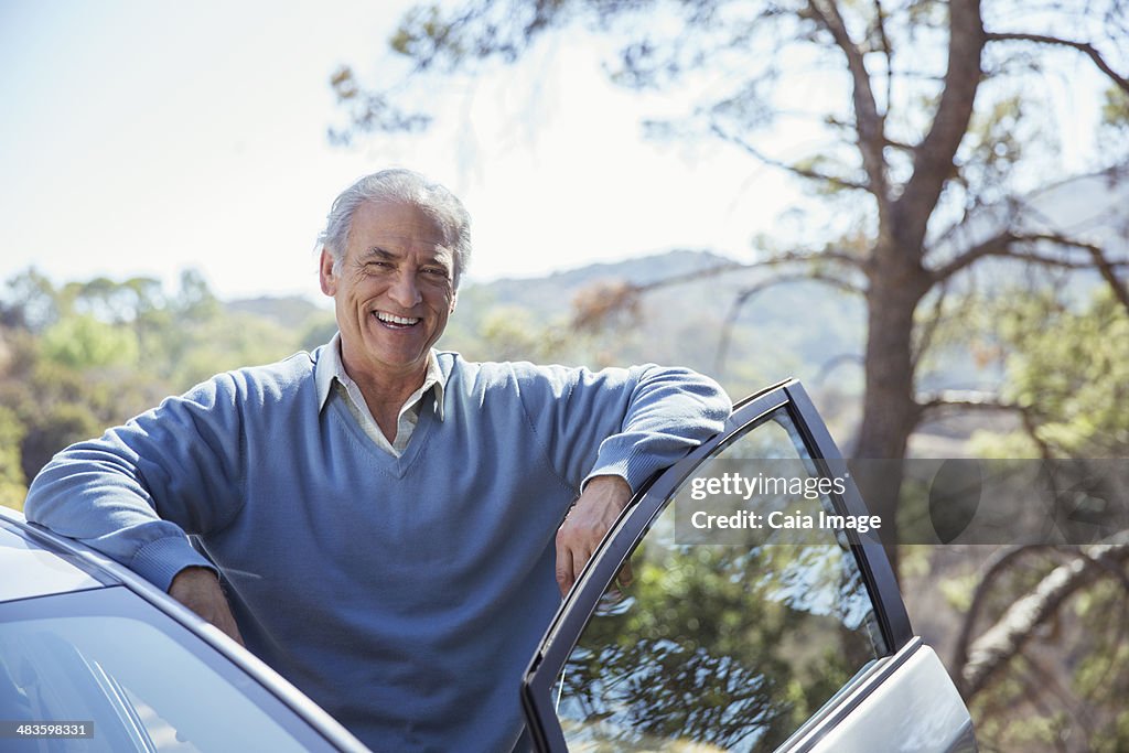 Retrato de feliz hombre mayor apoyarse en automóvil