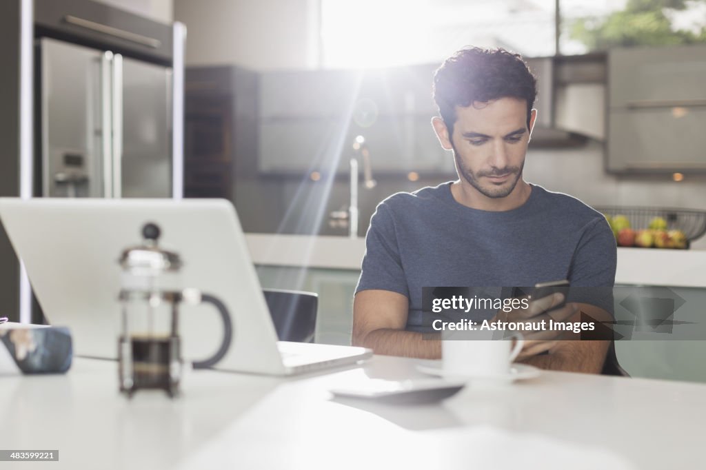 Man texting with cell phone at kitchen table