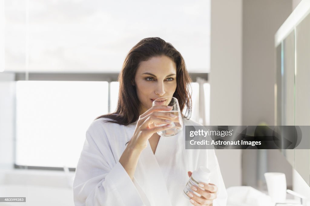Woman taking medication with water in bathroom