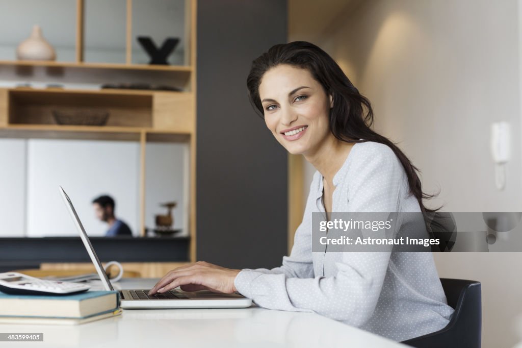 Portrait of smiling woman using laptop at table