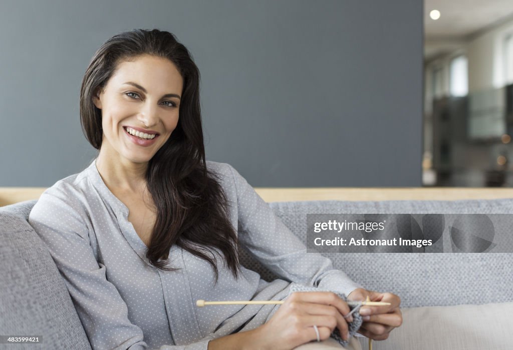 Portrait of smiling woman knitting on sofa