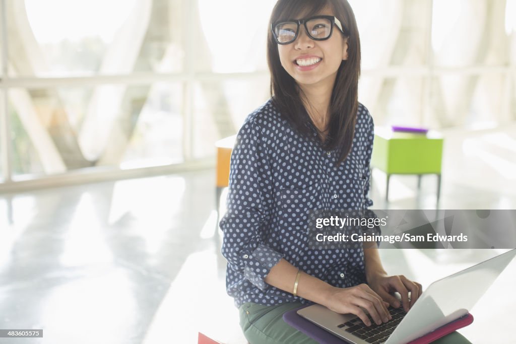Happy casual businesswoman using laptop in sunny office