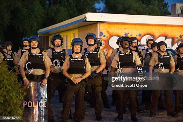 Police stand guard as demonstrators, marking the one-year anniversary of the shooting of Michael Brown, protest along West Florrisant Street on...