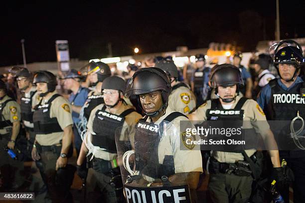 Police stand guard as demonstrators, marking the one-year anniversary of the shooting of Michael Brown, protest along West Florrisant Street on...