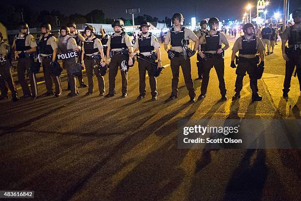 Police stand guard as demonstrators, marking the one-year anniversary of the shooting of Michael Brown, protest along West Florrisant Street on...