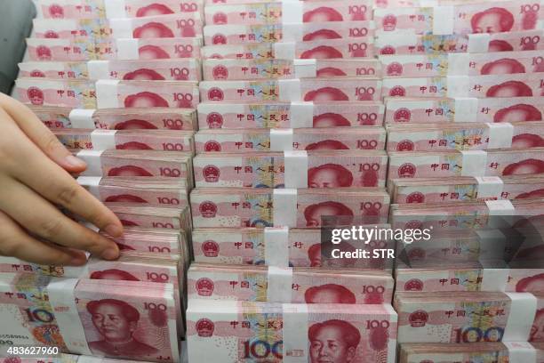 Teller counts yuan banknotes in a bank in Lianyungang, east China's Jiangsu province on August 11, 2015. China's central bank on August 11 devalued...