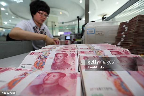 Teller counts yuan banknotes in a bank in Lianyungang, east China's Jiangsu province on August 11, 2015. China's central bank on August 11 devalued...