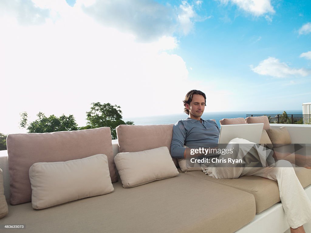 Man sitting on sofa outdoors with laptop and sky