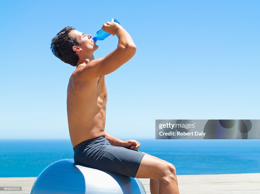 Hombre tomando un descanso de agua de estar en una pelota de ejercicio