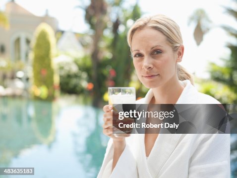 Women in bathrobe by a pool and drinking a water Women in bathrobe by a pool and drinking a water