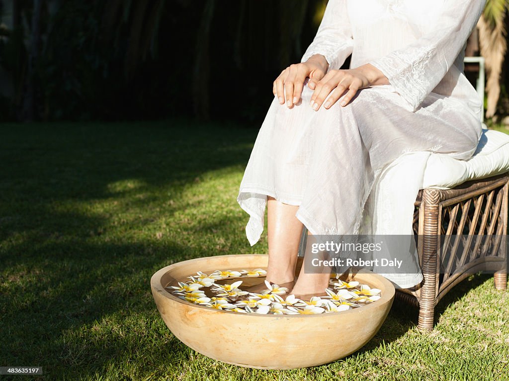 A woman's feet soaking in a bowl of water and flowers