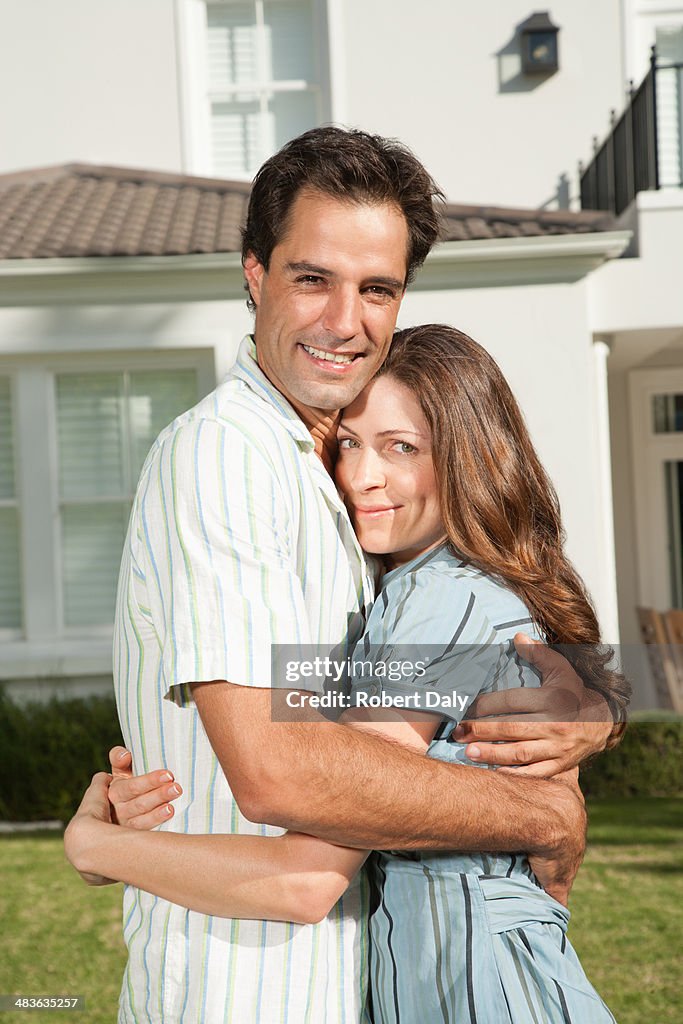 A couple embracing on the front lawn of a large home