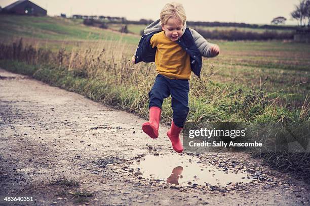 little boy jumping in a muddy puddle - pfütze stock-fotos und bilder