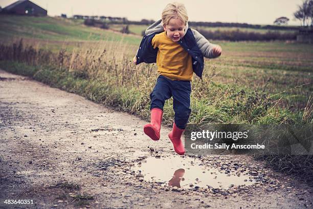 little boy jumping in a muddy puddle - puddle stock pictures, royalty-free photos & images