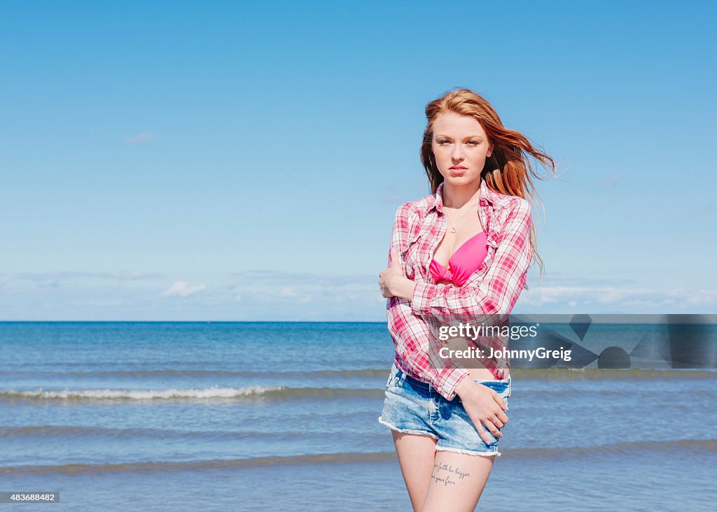 Beautiful red haired young woman standing by the sea