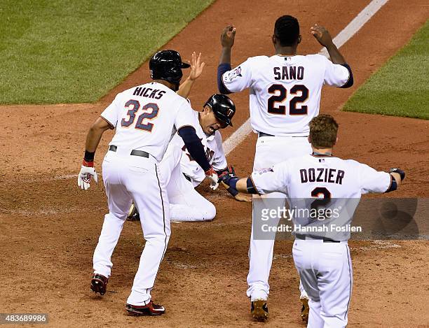 Kurt Suzuki of the Minnesota Twins celebrates sliding across home plate against the Texas Rangers during the ninth inning as teammate Aaron Hicks,...