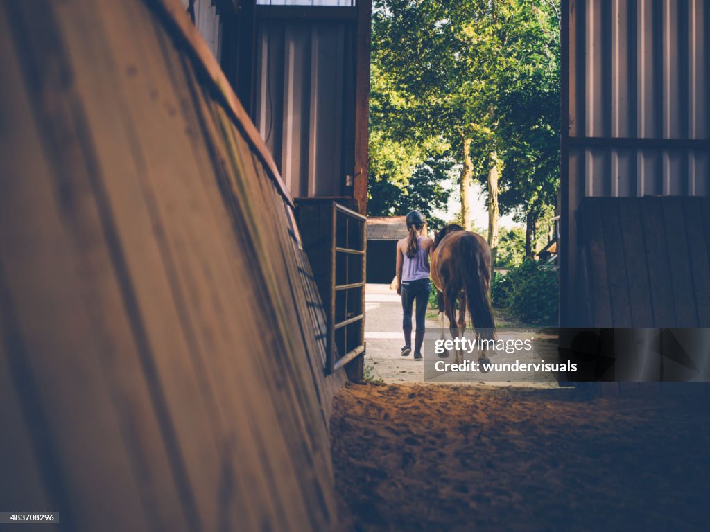 Girl leading her horse out of stables with vintage feel