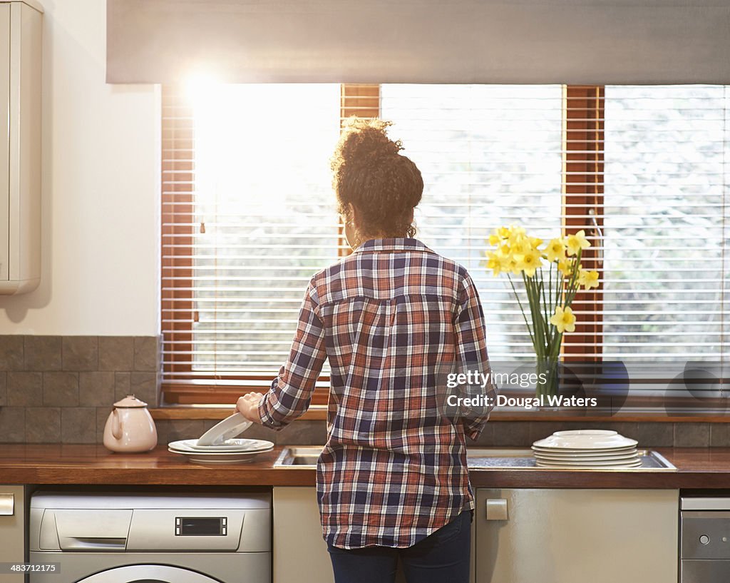 Woman washing up crockery in kitchen.