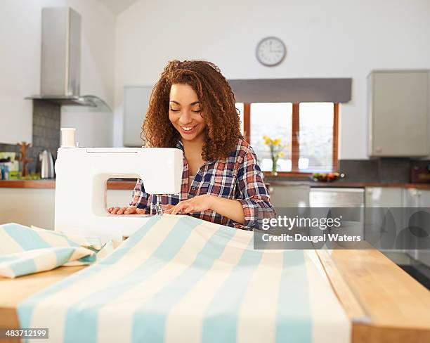 woman at kitchen table using sewing machine. - sewing machine imagens e fotografias de stock