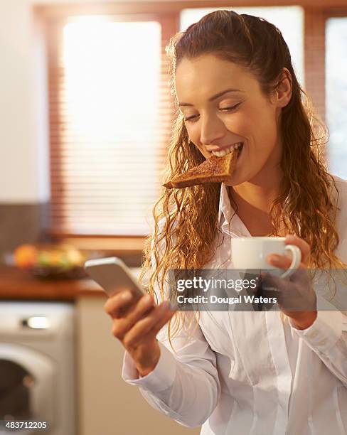 woman eating breakfast and using phone at home. - im mund tragen stock-fotos und bilder