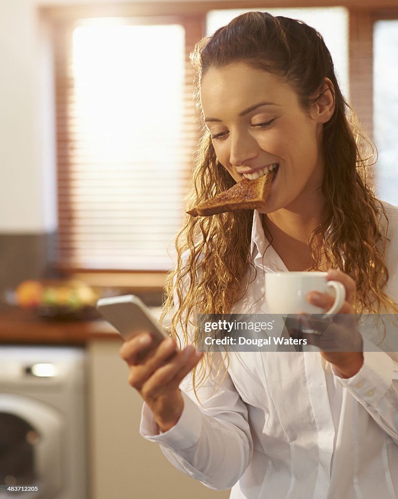 Woman eating breakfast and using phone at home.