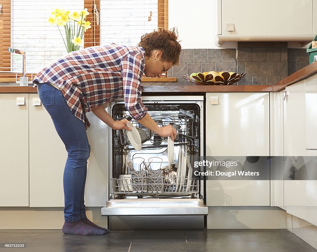 Woman unloading dish washer in kitchen.