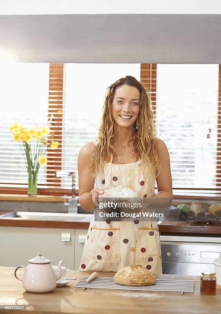 Woman in kitchen holding freshly baked bread.