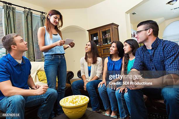 young woman reading card during game of charades with friends - mime stockfoto's en -beelden