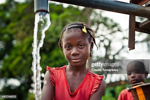 african girl by water pump - african girl drinking water stockfoto's en -beelden