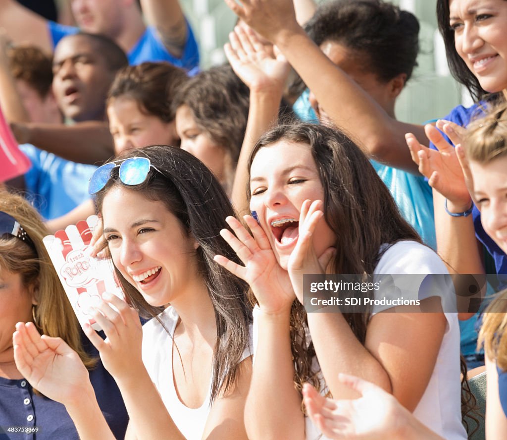 Excited crowd of fans cheering on team from stadium bleachers