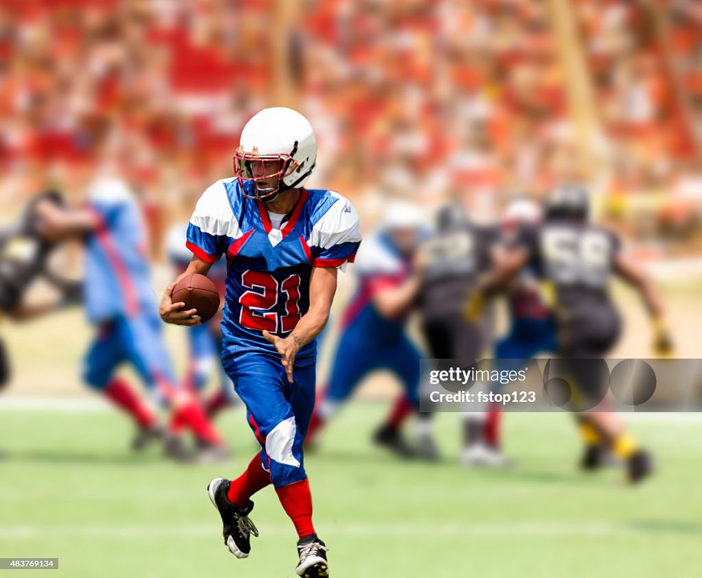 Football team's running back carries ball. Defenders. Stadium fans. Field.