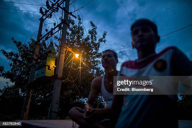People stand under a light powered by energy from a solar power microgrid at night in the village of Dharnai in Jehanabad, Bihar, India, on Thursday,...