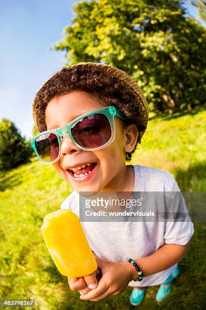 smiling boy holding orange popsicle in park - cream colored hat stock pictures, royalty-free photos & images