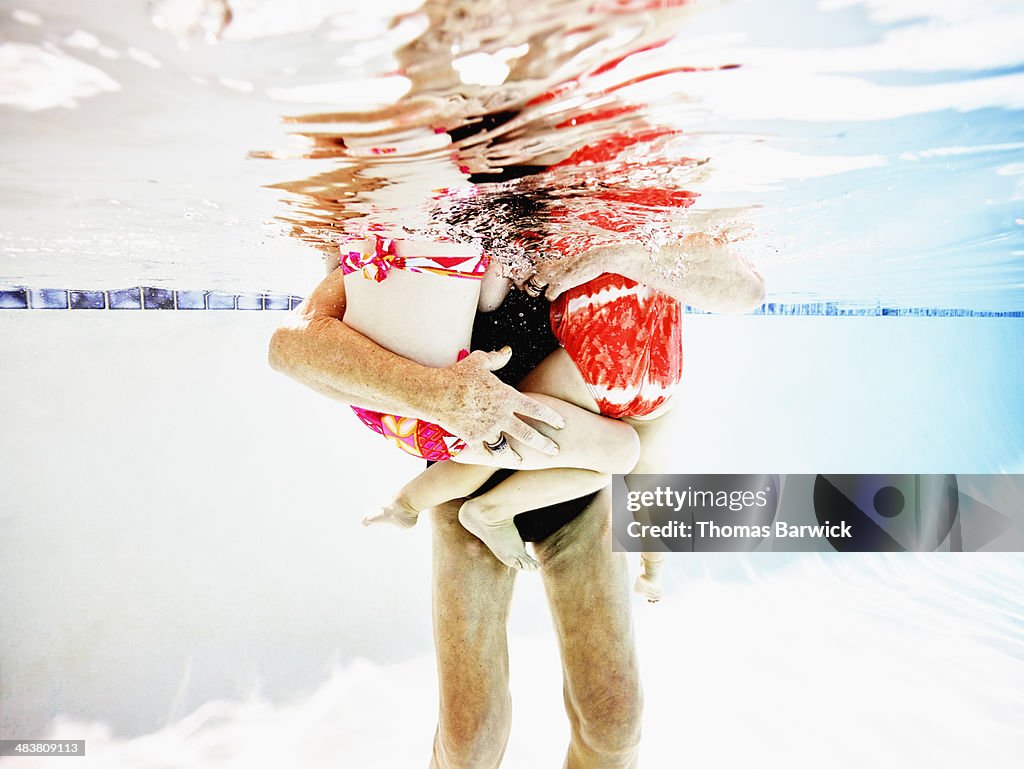 Senior woman holding granddaughters in pool