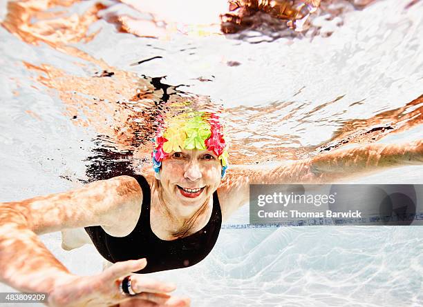 smiling senior woman swimming in pool - old woman in swimsuit stock-fotos und bilder