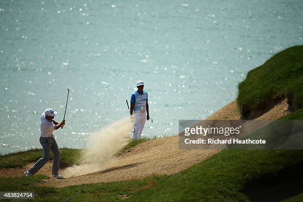 Dustin Johnson of the United States plays a bunker shot on the third hole as Rickie Fowler looks on during the first round of the 2015 PGA...