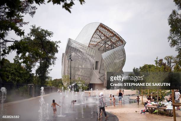 People enjoy the fountains at the Jardin d'Acclimatation with the Fondation Louis Vuitton in the background on August 13, 2015 in the northern part...