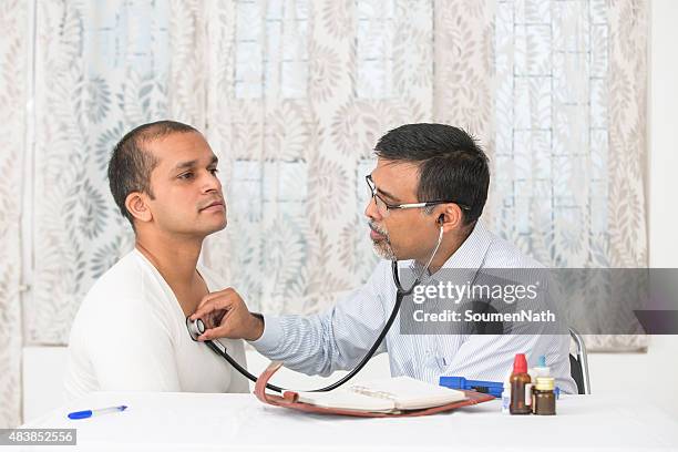 mature doctor examining a young patient with a stethoscope - cardiologist stock pictures, royalty-free photos & images