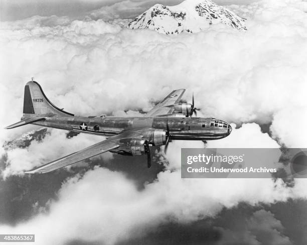 Air Force Boeing B-29 Superfortress bomber flying above the clouds and mountains, mid 1940s.