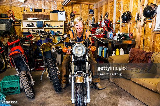 middle-aged woman with motorcycles in her garage. - racing garage stock pictures, royalty-free photos & images