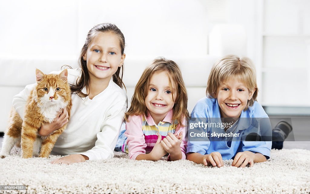 Kinder mit Katze liegen auf dem Teppich.
