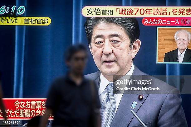 Man walks past a big screen showing a live broadcast of Japanese Prime Minister, Shinzo Abe as he delivers his WWII Anniversary Statement on August...