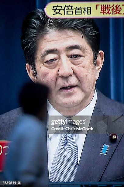 Man walks past a big screen showing a live broadcast of Japanese Prime Minister, Shinzo Abe as he delivers his WWII Anniversary Statement on August...