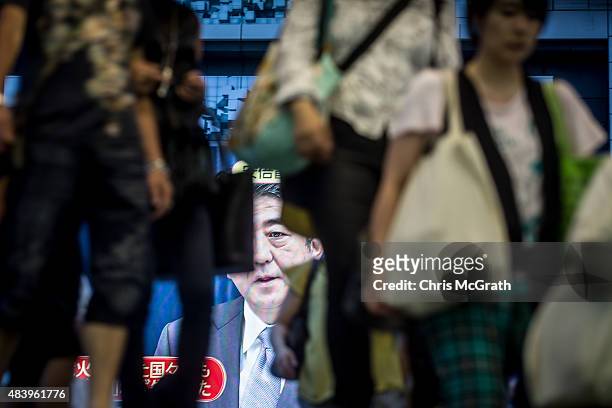 Pedestrians enter a train station in front of a big screen showing a live broadcast of Japanese Prime Minister,Shinzo Abe as he delivers his WWII...