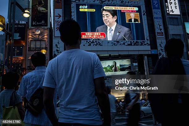 People watch a big screen showing a live broadcast of Japanese Prime Minister, Shinzo Abe as he delivers his WWII Anniversary Statement on August 14,...