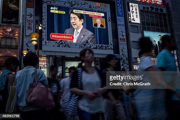 Pedestrians walk past a big screen showing a live broadcast of Japanese Prime Minister,Shinzo Abe as he delivers his WWII Anniversary Statement on...