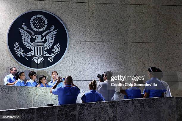 Embassy employees pose for photograph underneath the seal of the United States after it was hung a few hours before the official flag-raising...