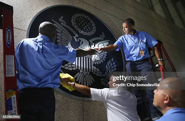 Embassy employees clean the seal of the United States after hanging it on the outside of the building a few hours before the ceremonial flag-raising...