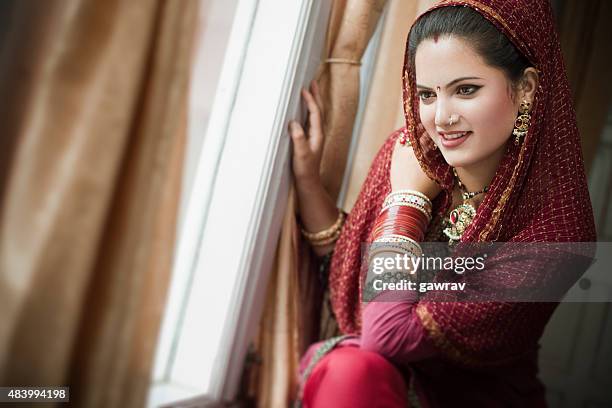 beautiful newly married happy indian young woman sitting near window. - indian bridal makeup stock pictures, royalty-free photos & images